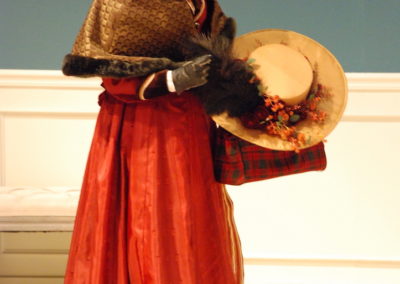 woman standing, holding her traveling hat and bag