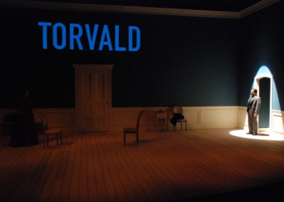 man in spotlight, text projected onto wall that reads "Torvald"