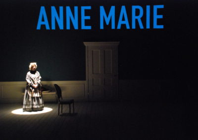 woman in spotlight, text projected onto wall that reads "Anne Marie"