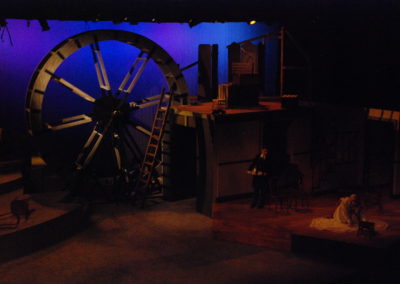 two people in a dark scene on the right, full stage view including mill wheel