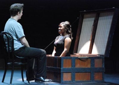 a man sitting in a chair talking to a woman who is inside of a steamer trunk