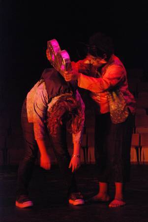 a woman with a giant turnkey coming out of her back bent over, another woman trying to turn the key with both of her hands