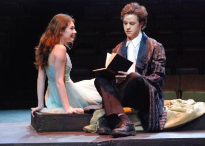 a woman sits on a cushio listening to a man who is squatting next to her reading from a book