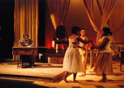 a woman at a sewing machine on stage right, three women folding fabric stage left