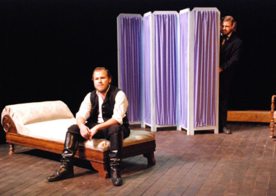 a man sitting on a chaise lounge, another man hiding behind a dressing screen upstage and spying on the first man