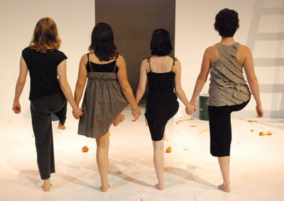 four women standing in a row holding hands and facing upstage