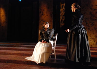 a woman sits in a chair talking to another woman who stands next to her