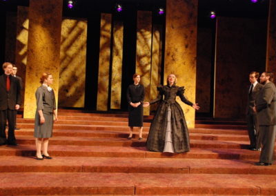 a woman stands center making grand gestures, six people stand around watching her
