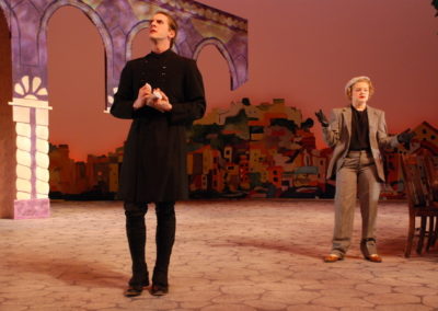 a man stands downstage talking to a woman who is behind him and to his left