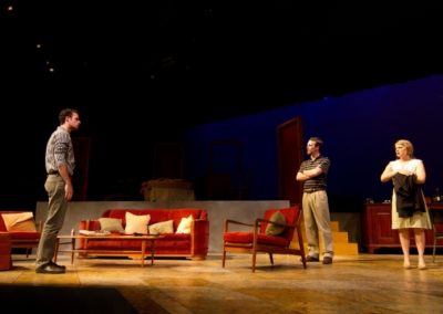 three people standing and talking, one man on stage right, a man and a woman on stage left