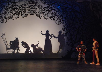 large silhouette of 5 people in various poses on the backdrop, 2 men standing and talking downstage left in front of backdrop