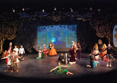 full stage tableau, twenty-two people arranged in small groups holding various poses spread out across the stage