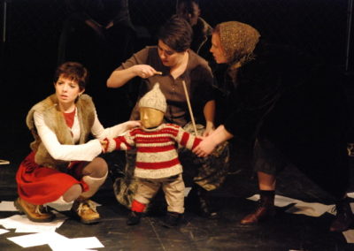 two women pulling on opposite arms of a child puppet and the child puppet operator