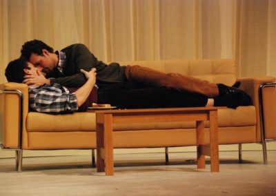 two men laying on a couch together, holding each other romantically