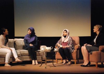 four women sitting and talking, two center women wearing hijabs