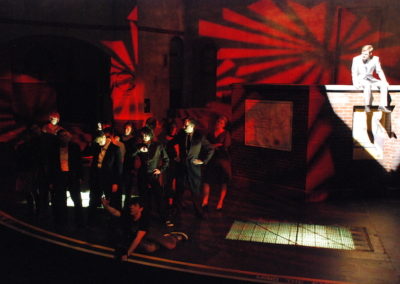 man in spotlight on a platform, group of people in shadows on floor