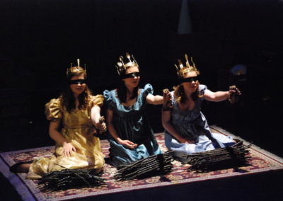 three blindfolded women kneeling wearing crowns, left arms outstretched, bundles of sticks in front of each one