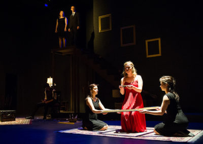 three women performing a ritual on the floor while two people watch from a platform above