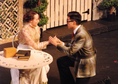 woman sitting on chair in a garden, man on one knee in front of her holding her hands