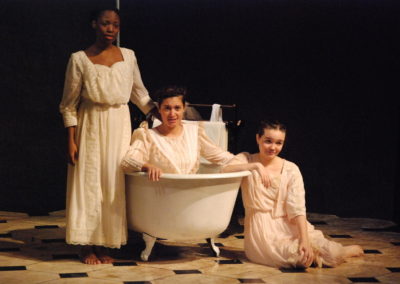 one woman sitting in a bathtub, two others next to the bathtub, one sitting on the floor, one standing