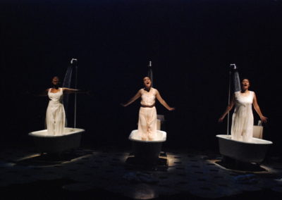 three women, each standing in a vintage bathtub, with showers running
