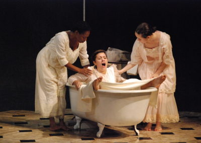 woman pretending to give birth while sitting in a bathtub, two woman standing and helping
